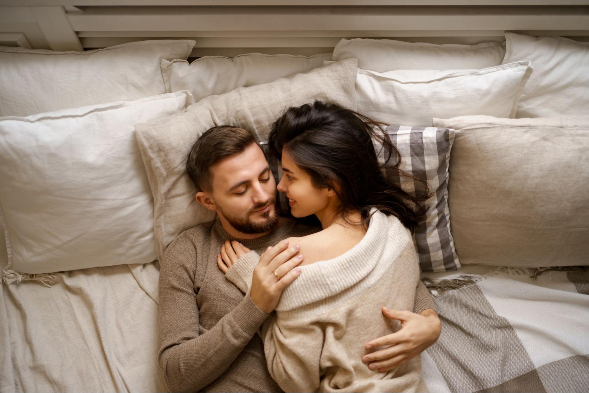  A man and woman hugging closely under the covers.