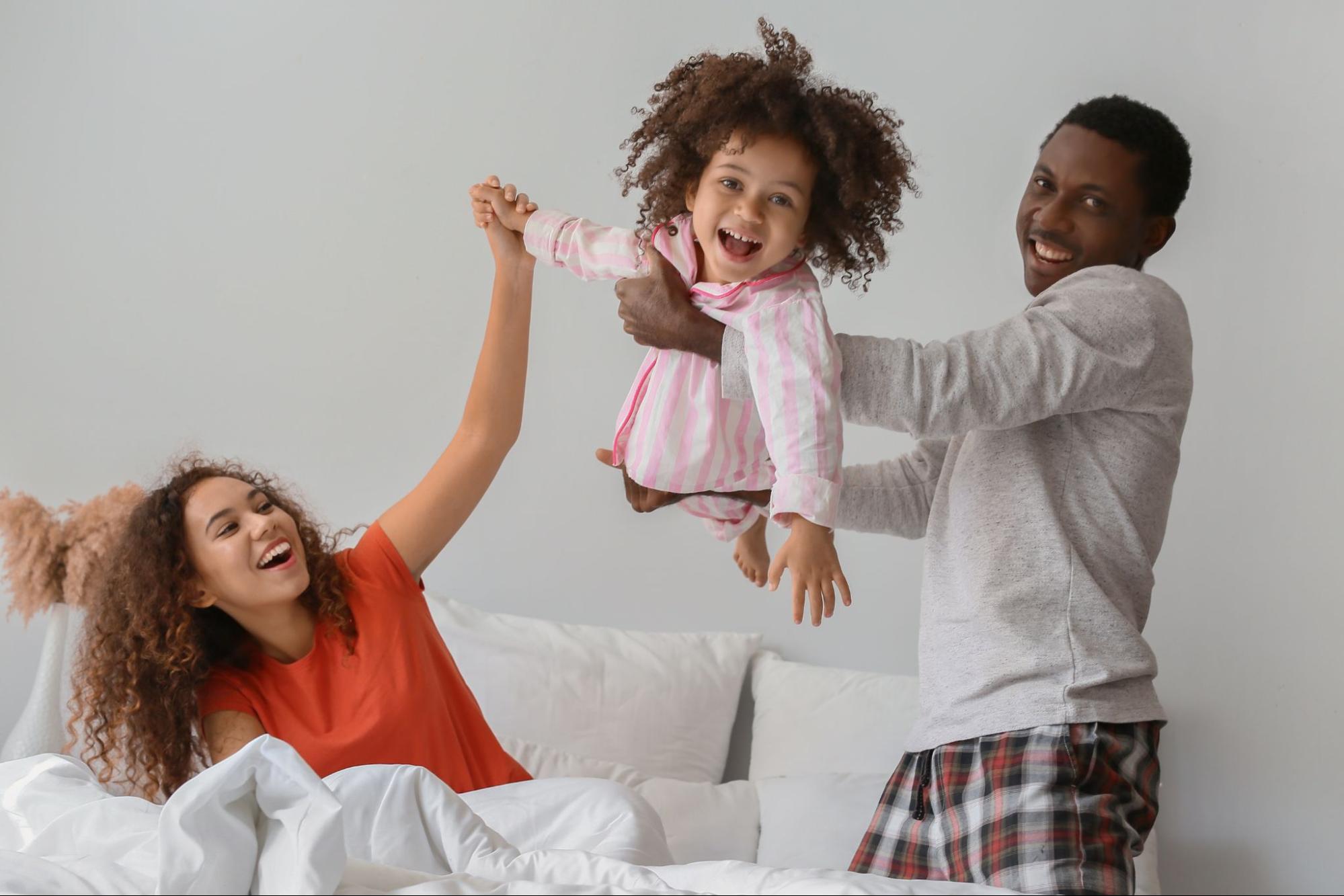 A joyful family playing on a bed with their child