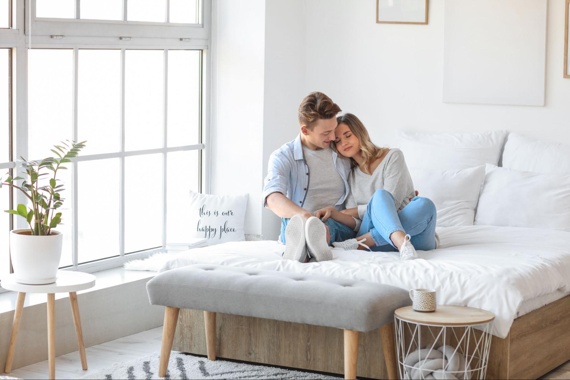 Two people relaxing on a bed in a bedroom with white walls.